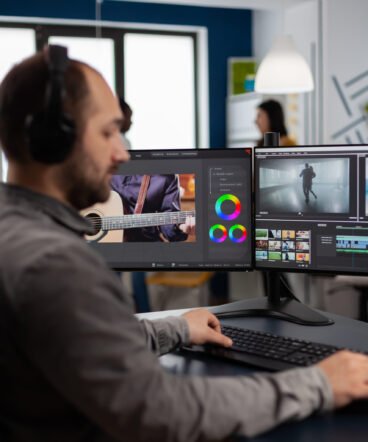 Graphic video production working on pc with two displays editing video Graphic video production working on pc with two displays editing video and audio footage sitting in creative workplace. Video maker employee processing film montage in digital multimedia company